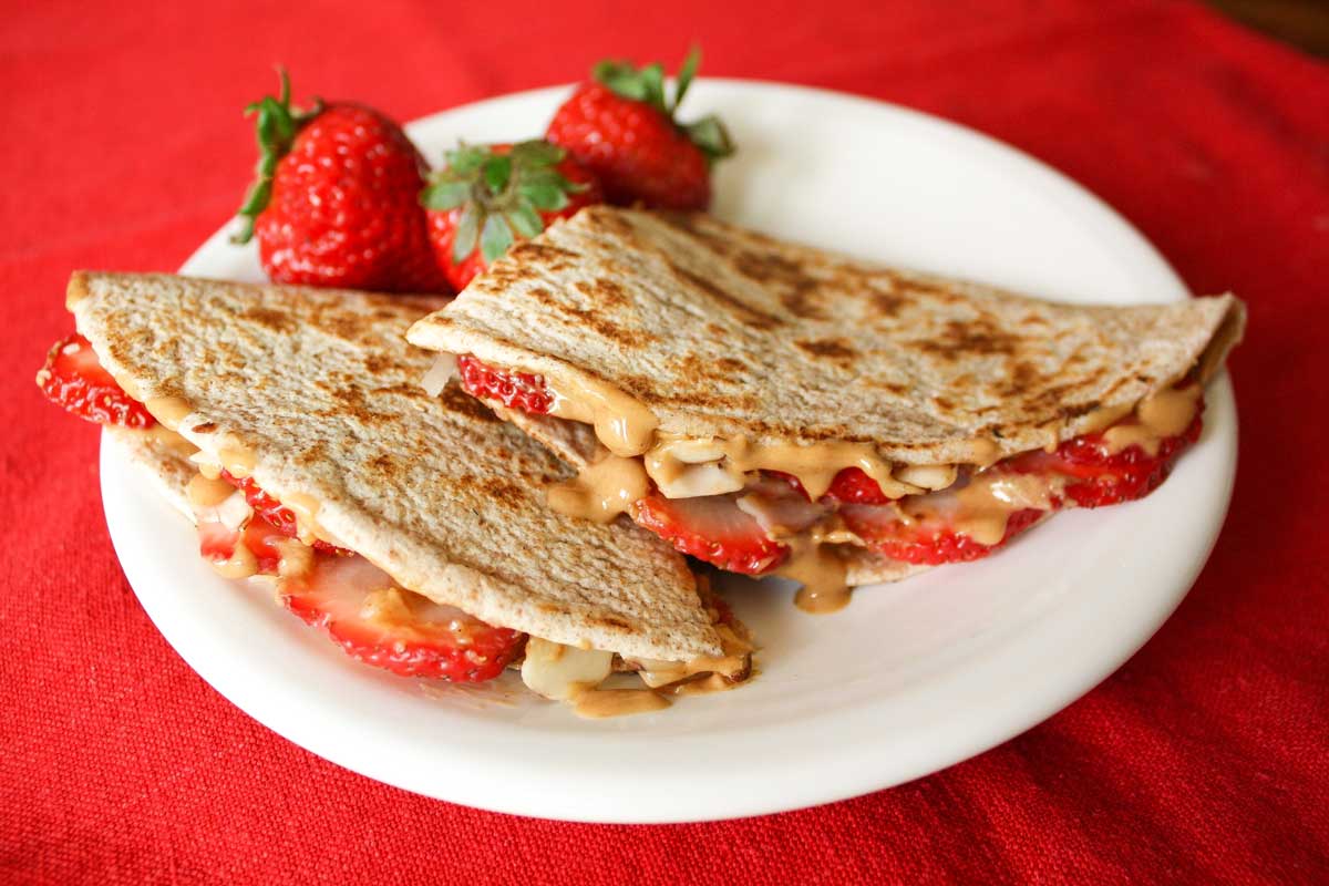 2 grilled tortilla wedges on white plate and red cloth, warm peanut butter dripping, garnish of 3 fresh strawberries.