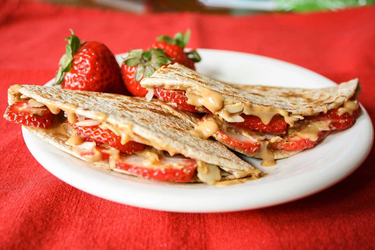Side view of stuffed tortilla wedges on plate with warm, drippy peanut butter and fresh strawberries.
