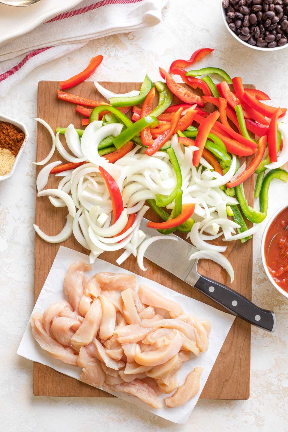 Flatlay of chicken, onion and peppers, all sliced into fajita strips on cutting board.