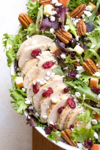 Overhead closeup of the sliced chicken fanned on the greens with pecans, cheese and fruit sprinkled on top.