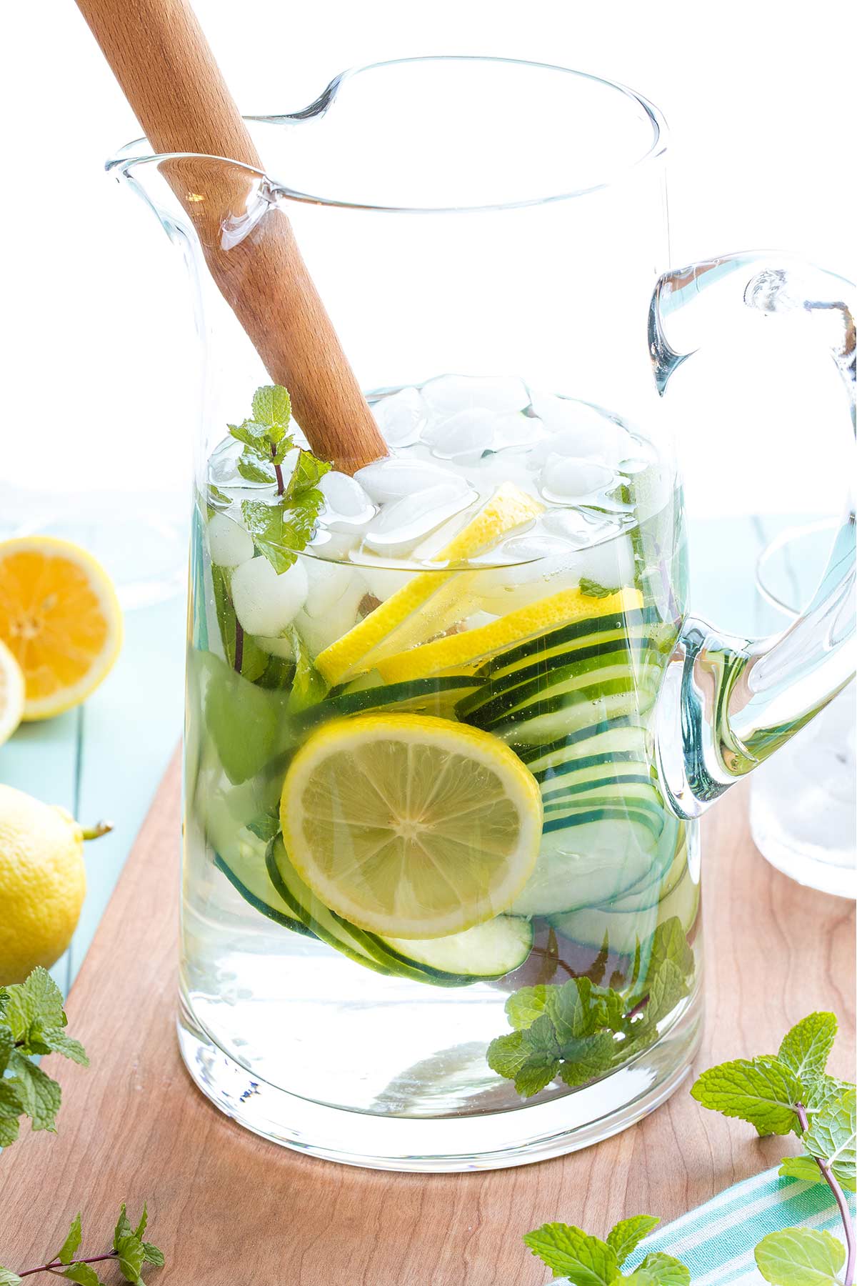 Side view of glass pitcher of water, so you can see the floating mint sprigs and slices of lemon and cucumbers.