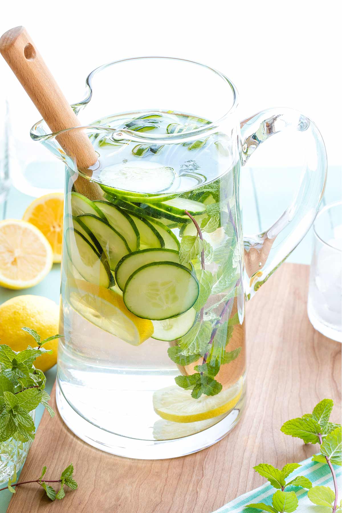 Glass pitcher full of water and infusing ingredients, with wooden spoon in for stirring.