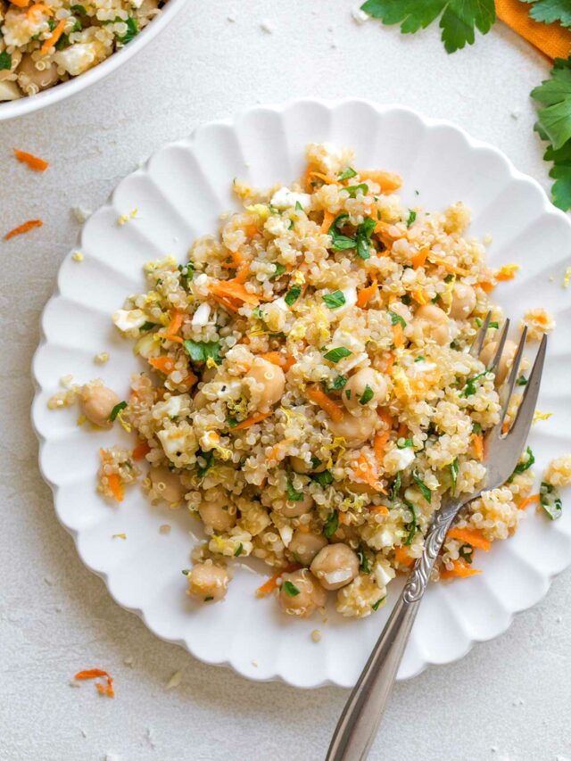 Flatlay of Quinoa Chickpea Salad on decorative little white plate with fork; salad bowl and parsley sprig nearby.