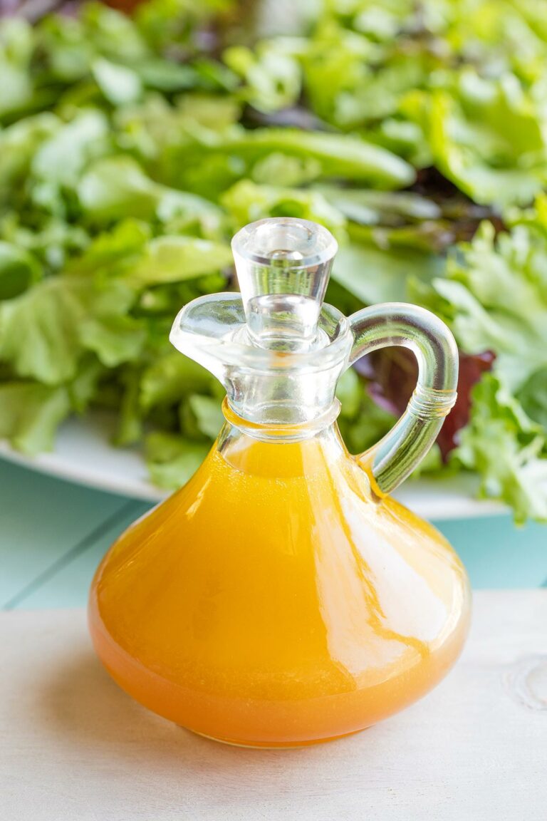 Vinaigrette in stoppered cruet with large platter of salad behind.