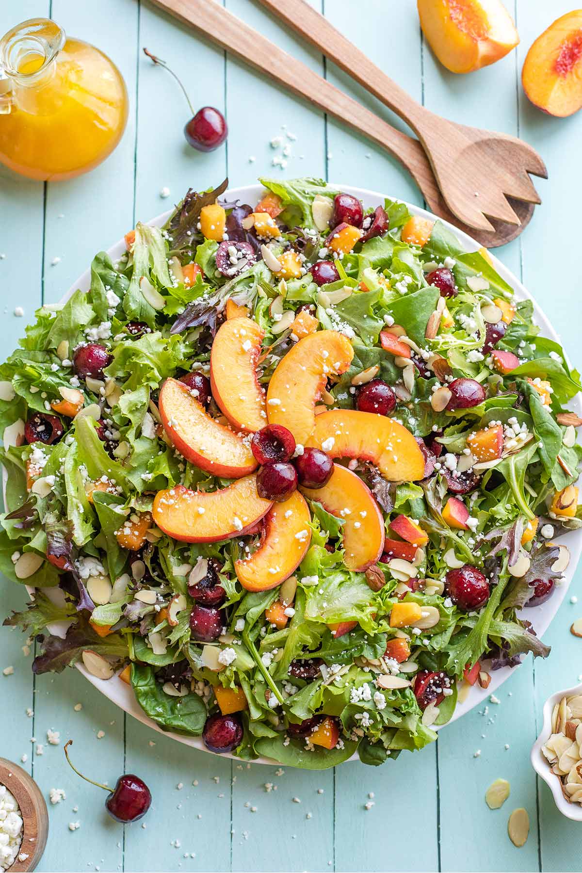 Overhead of salad with peaches and cherries, with salad servers and glass pitcher of White Balsamic Vinaigrette.