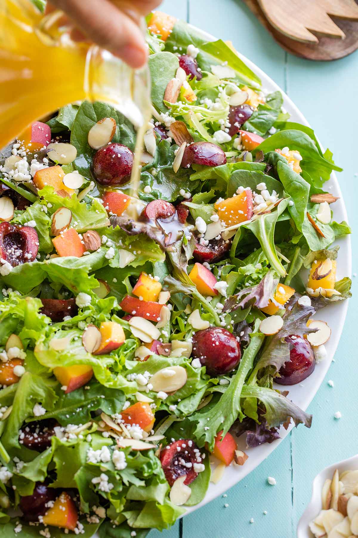 Hand pouring White Balsamic Dressing from cruet onto salad below.