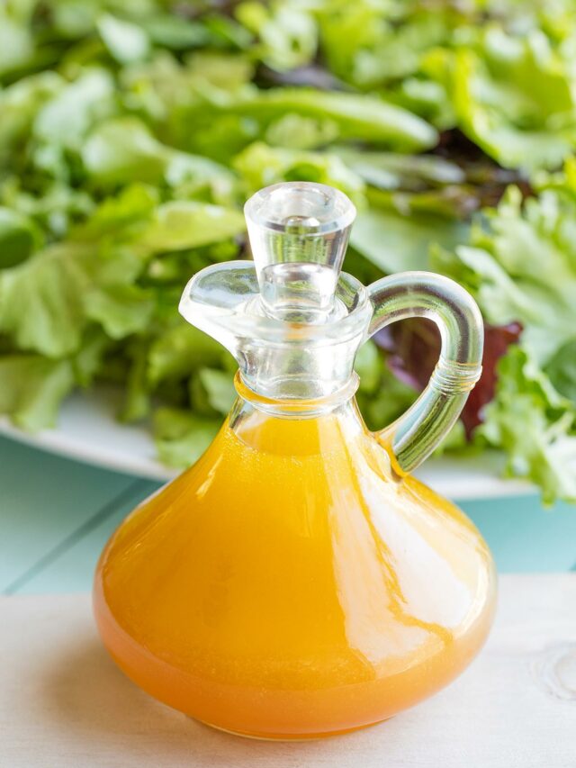 Vinaigrette in stoppered cruet with large platter of salad behind.