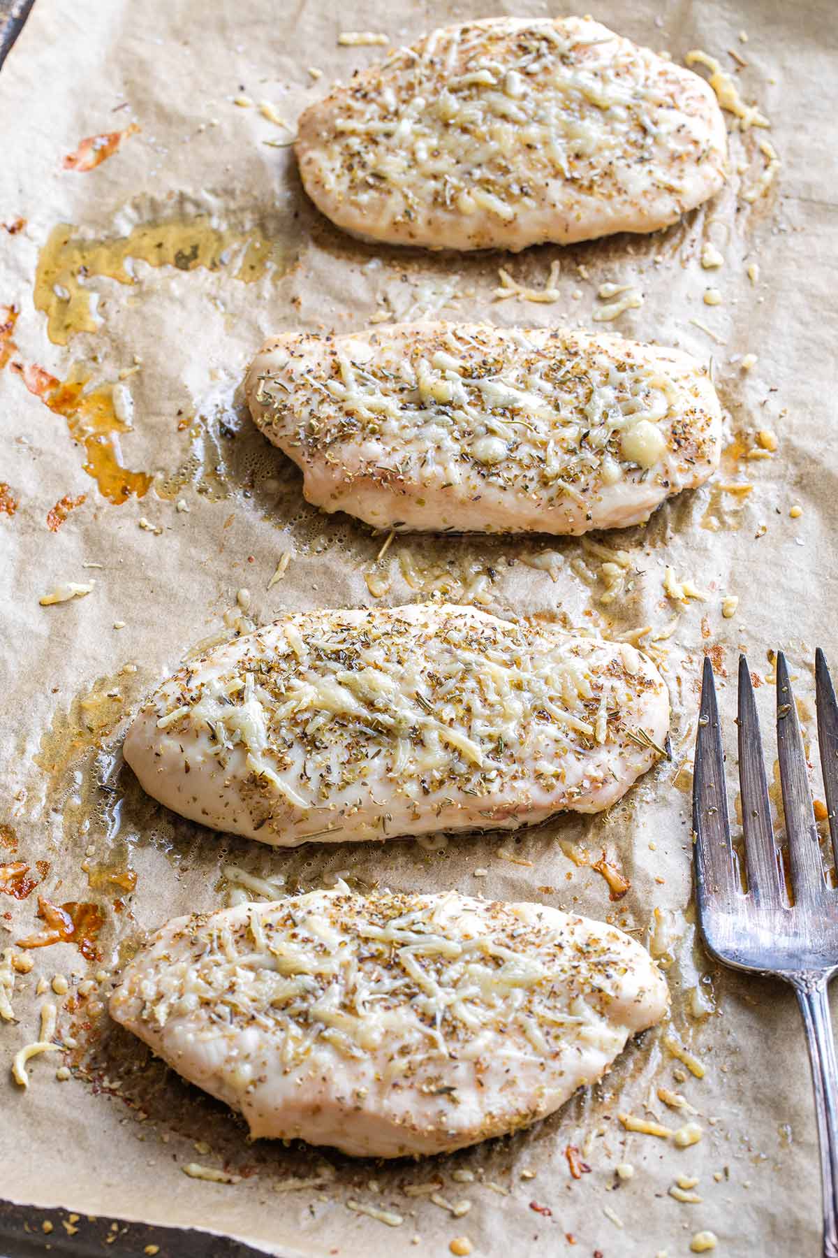 Baked chicken still by itself on baking sheet with large meat fork alongside.