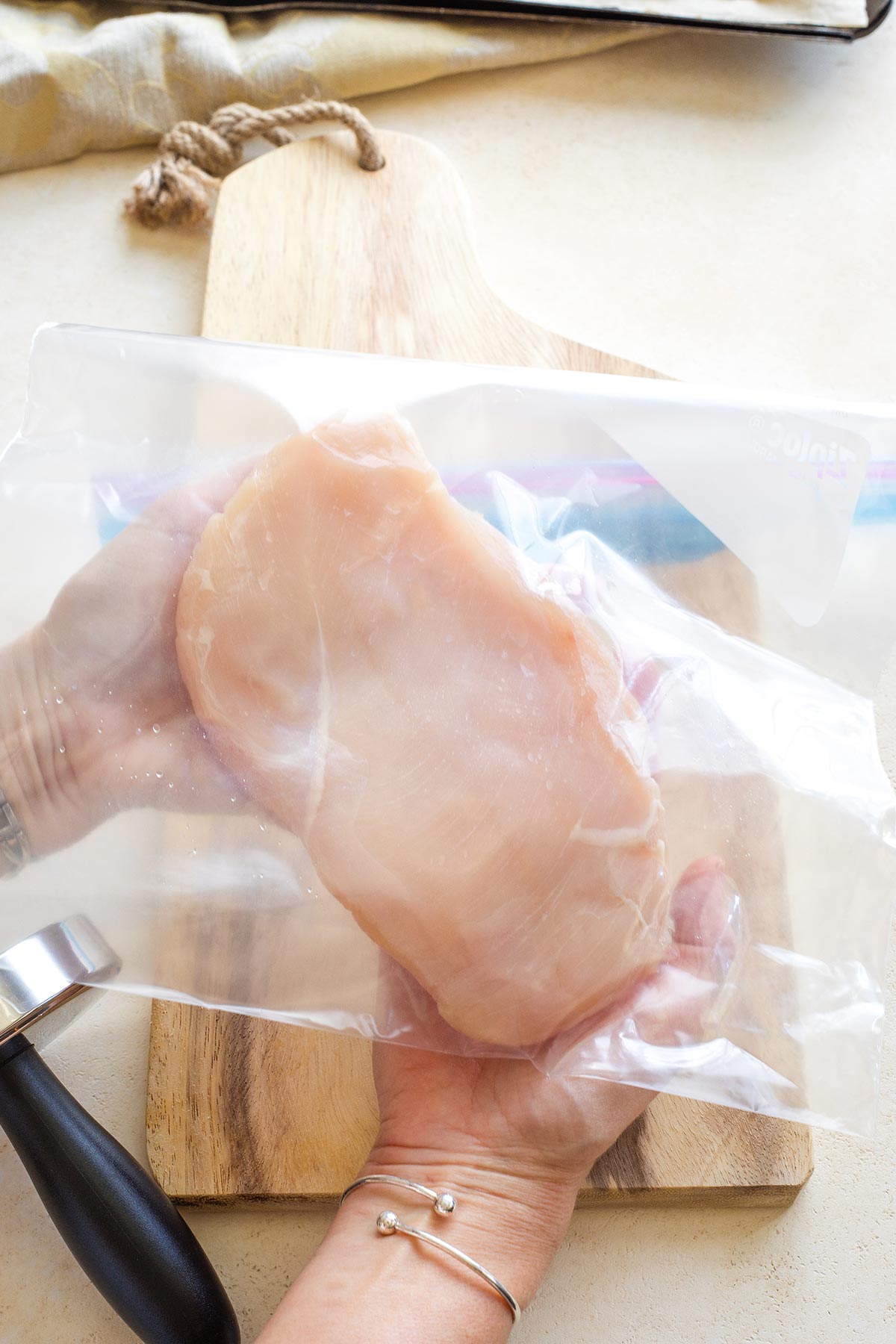 Two hands holding up a flattened chicken breast in plastic bag.