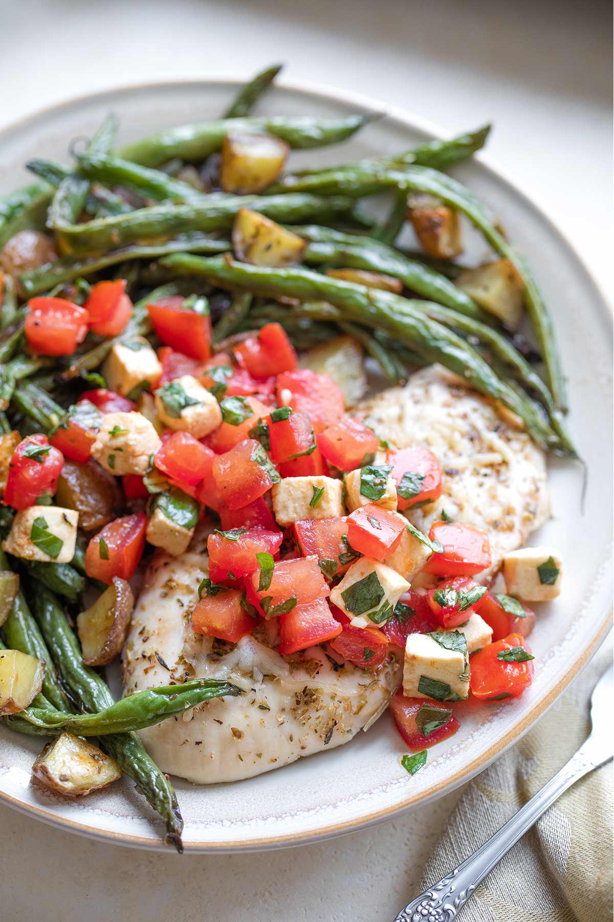 Closeup of one dinner plate with baked vegetables arranged around chicken and topped with topping.