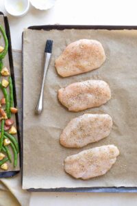 Overhead of chicken seasoned with Italian spices, arranged on sheet pan before being baked.