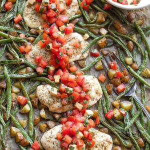 Closeup overhead of baked chicken nestled in the veggies with Italian topping spooned across.