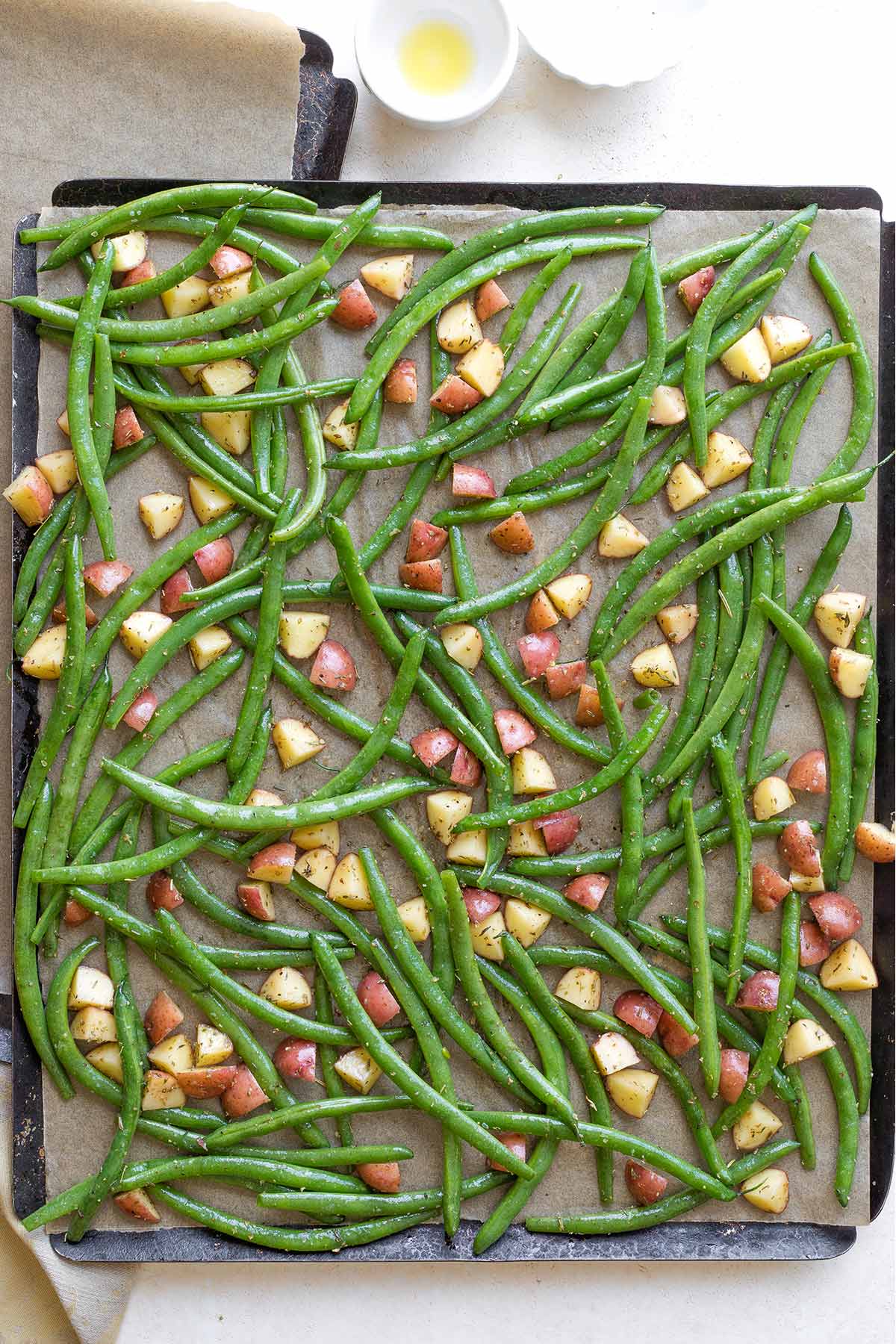 Overhead of seasoned veggies spread out on sheet pan before being baked.