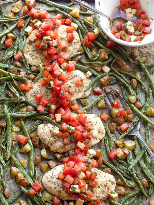 Flatlay of baked chicken and vegetables combined on 1 sheet pan with topping and serving fork.