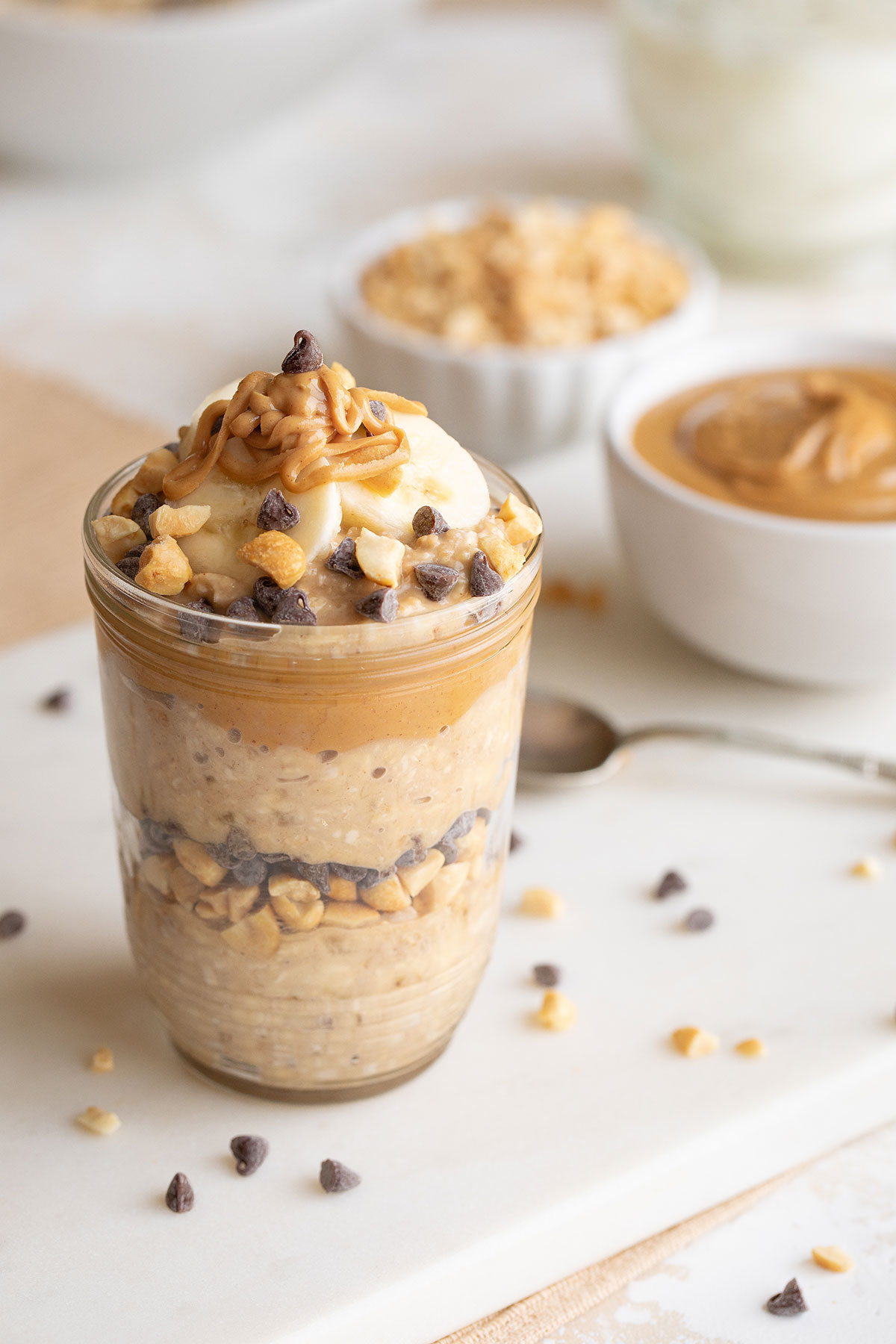 Jar full of oats, layered with peanuts and mini chocolate chips, with banana slices and peanut butter drizzle on top.