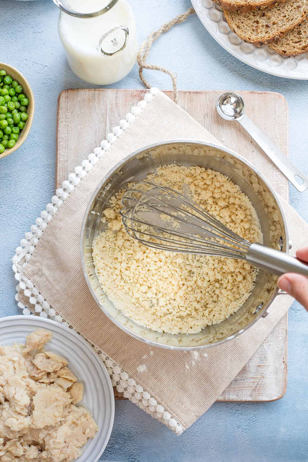 Hand whisking in pan as flour separates into coarse crumbs.