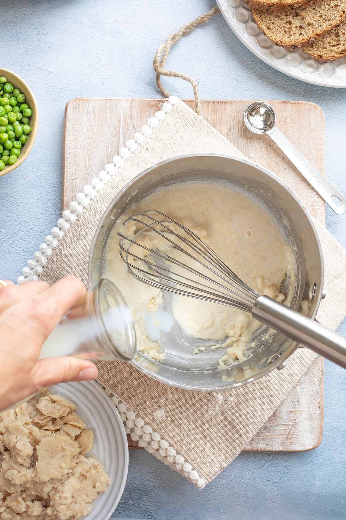 Hand pouring in milk to begin making creamed sauce.