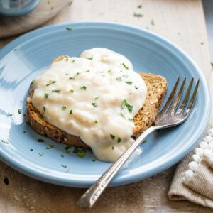 Closeup side view of tuna cream sauce cascading over a piece of toast on light blue plate with fork.