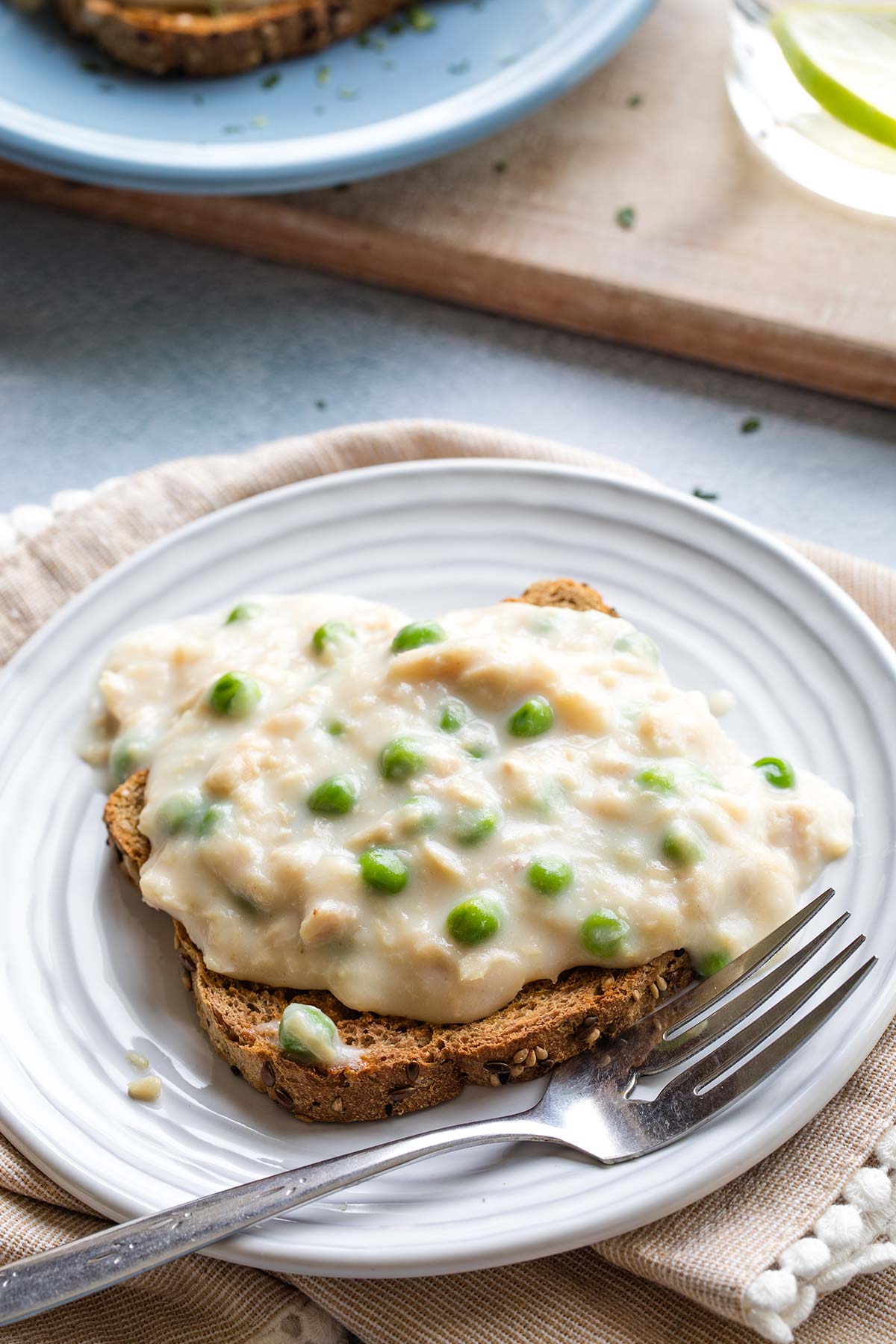 Closeup of the creamed tuna sauce studded with peas, over a piece of toast on a ridged plate with fork.