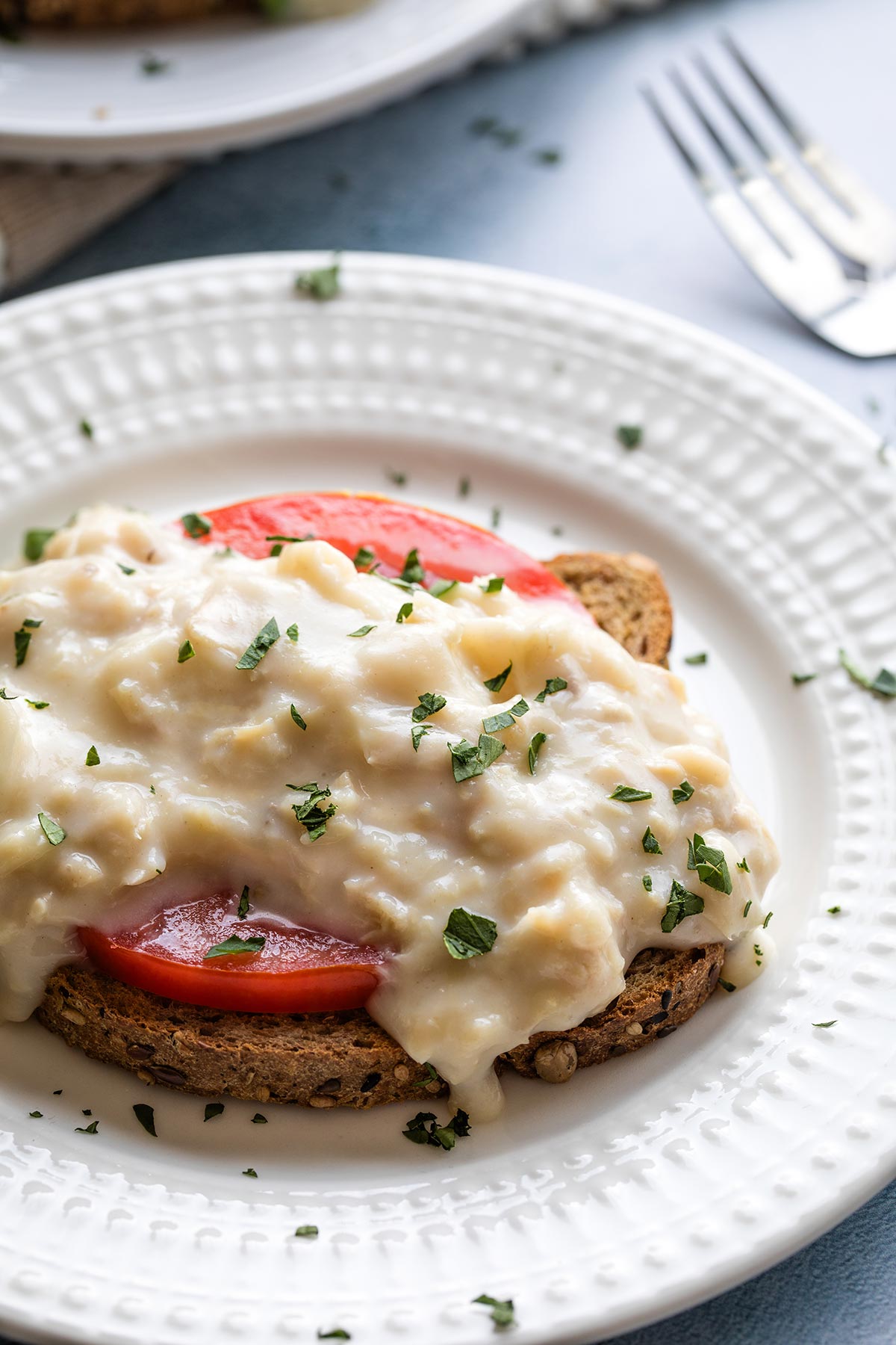 Closeup of the creamed tuna served on top of a tomato slice and sprinkled with bit of fresh parsley.