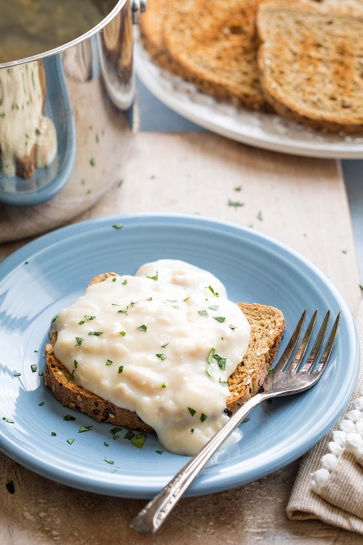 "Basic" recipe with creamed tun spooned over a piece of toast on a blue plate with fork; pan and toast sliced in background.