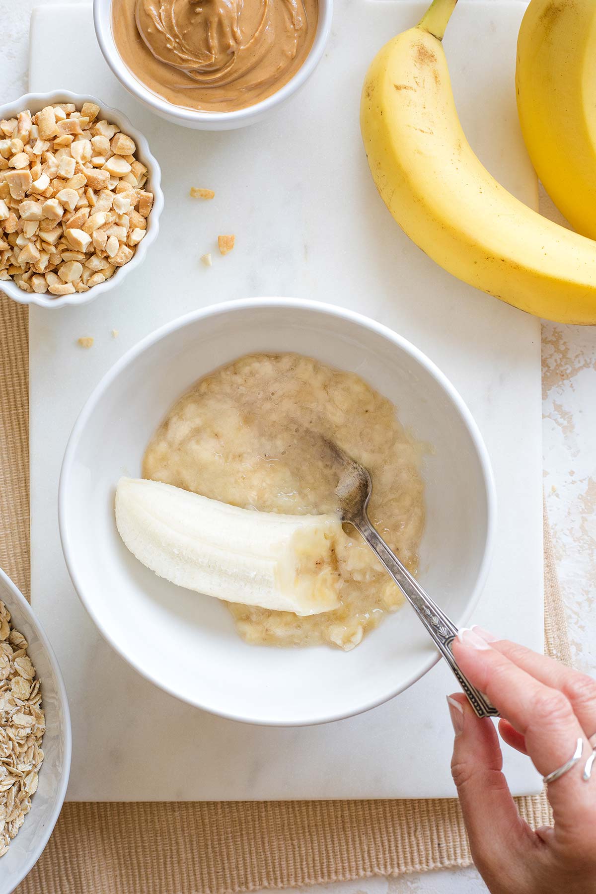 Hand using fork to mash banana in white bowl.