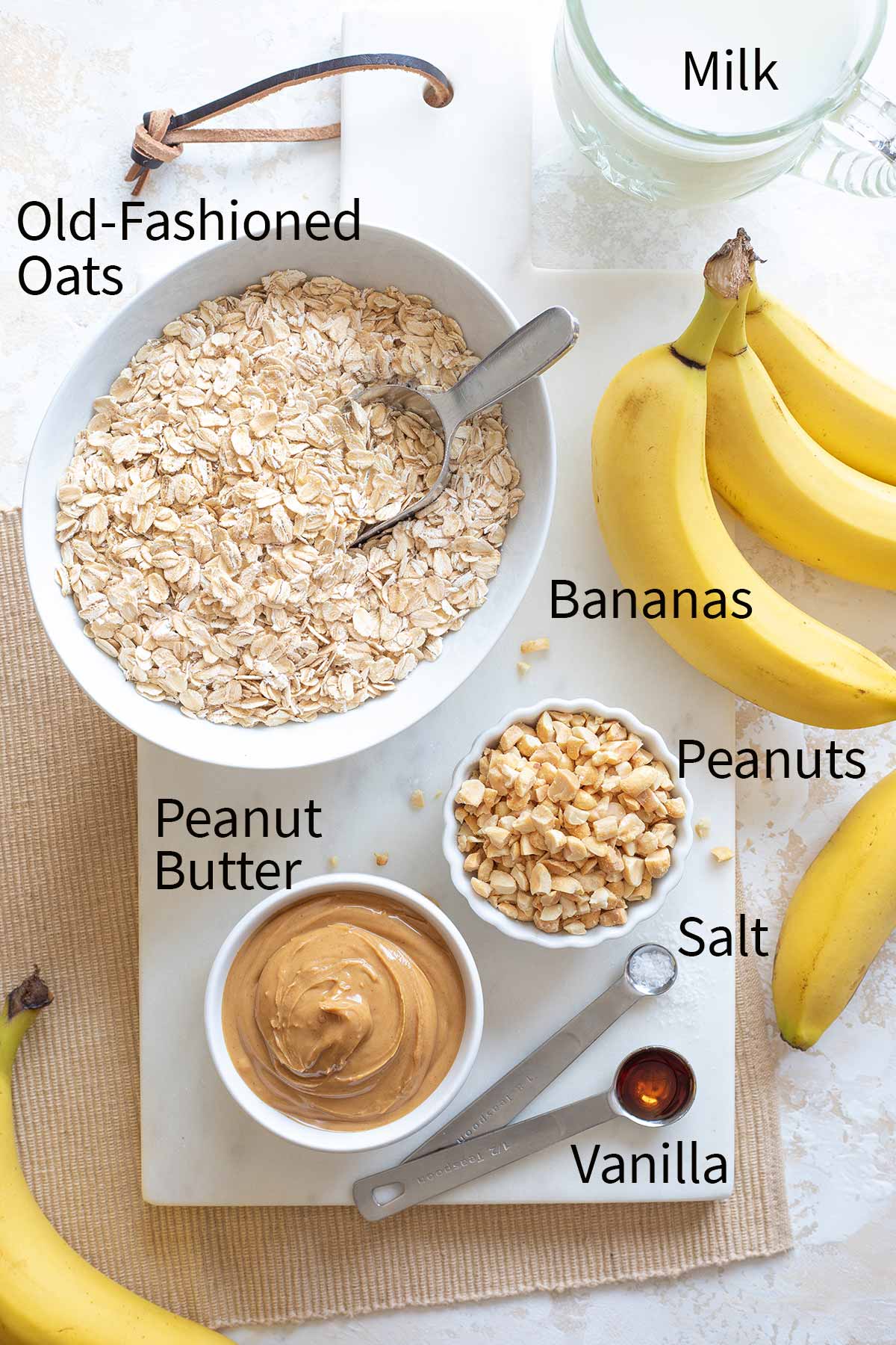 Flatlay of ingredients with labels (clockwise) "Old-Fashioned Oats, Milk, Bananas, Peanuts, Salt, Vanilla, Peanut Butter".