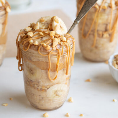 Side view of one filled jar topped with nuts bananas, with a spoon stuck in.