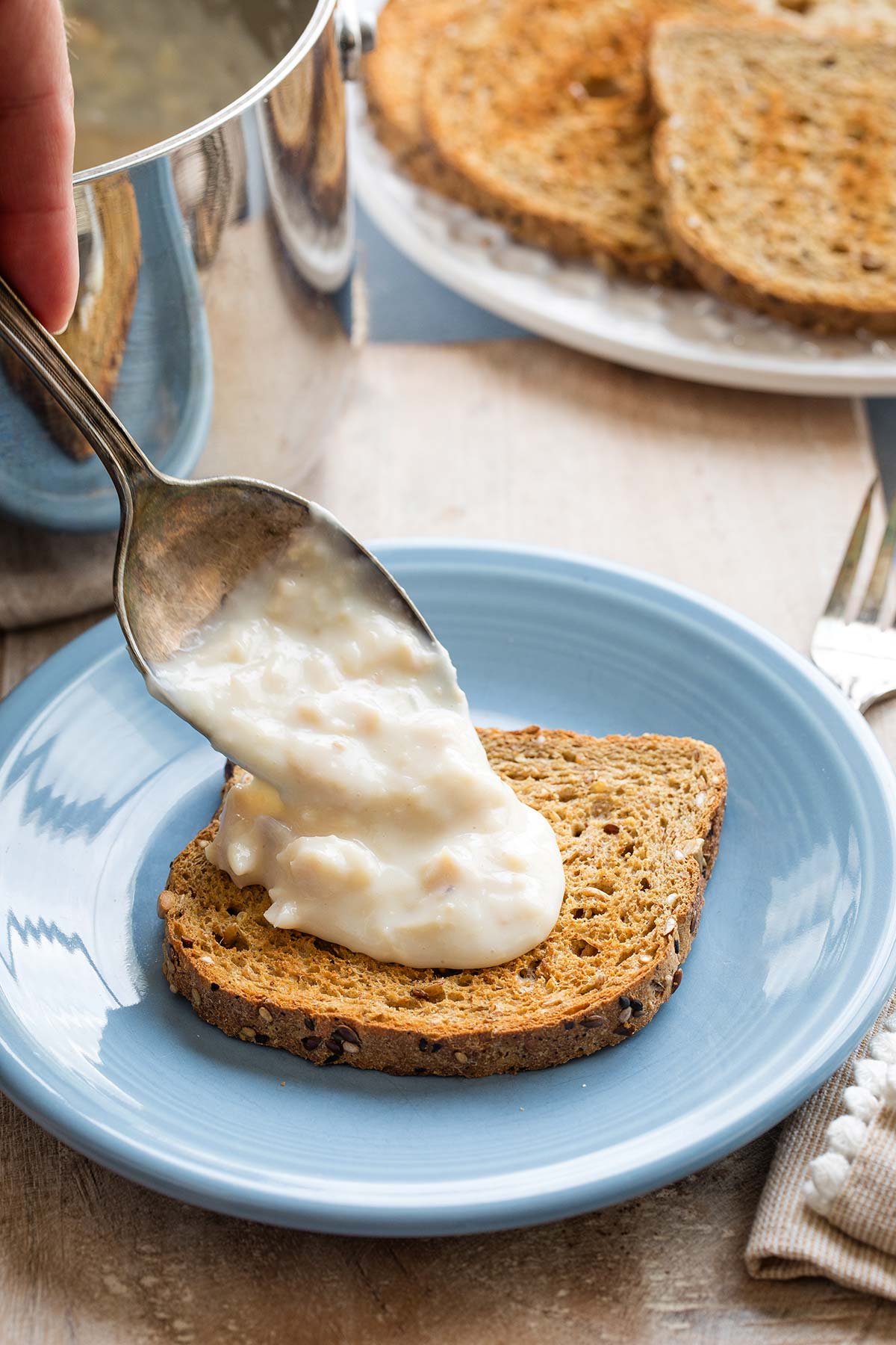 Serving spoon dribbling creamed tuna sauce over a piece of toast on a blue plate.