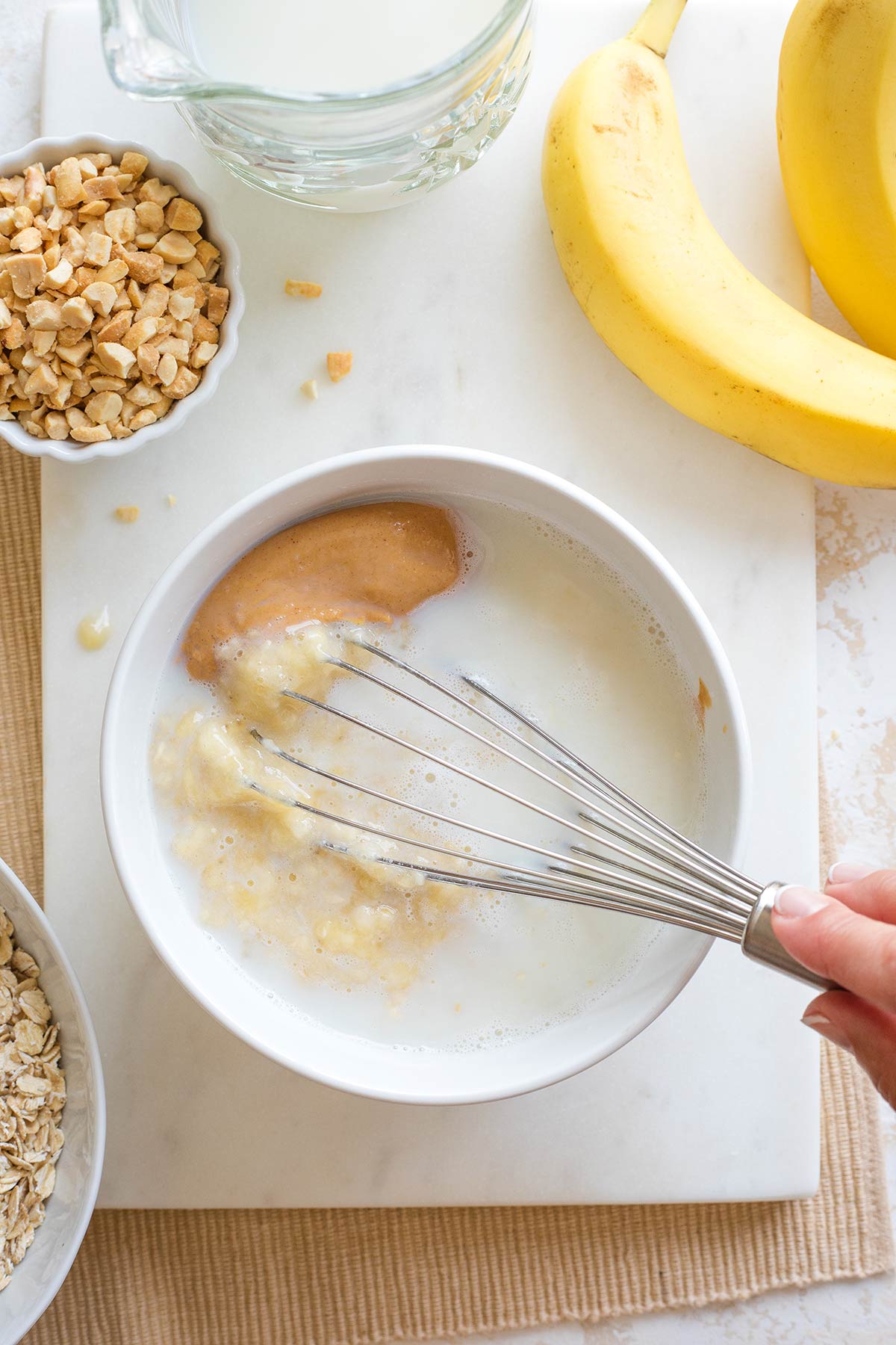 Hand using whisk to begin mixing the milk, banana and peanut butter together in bowl.