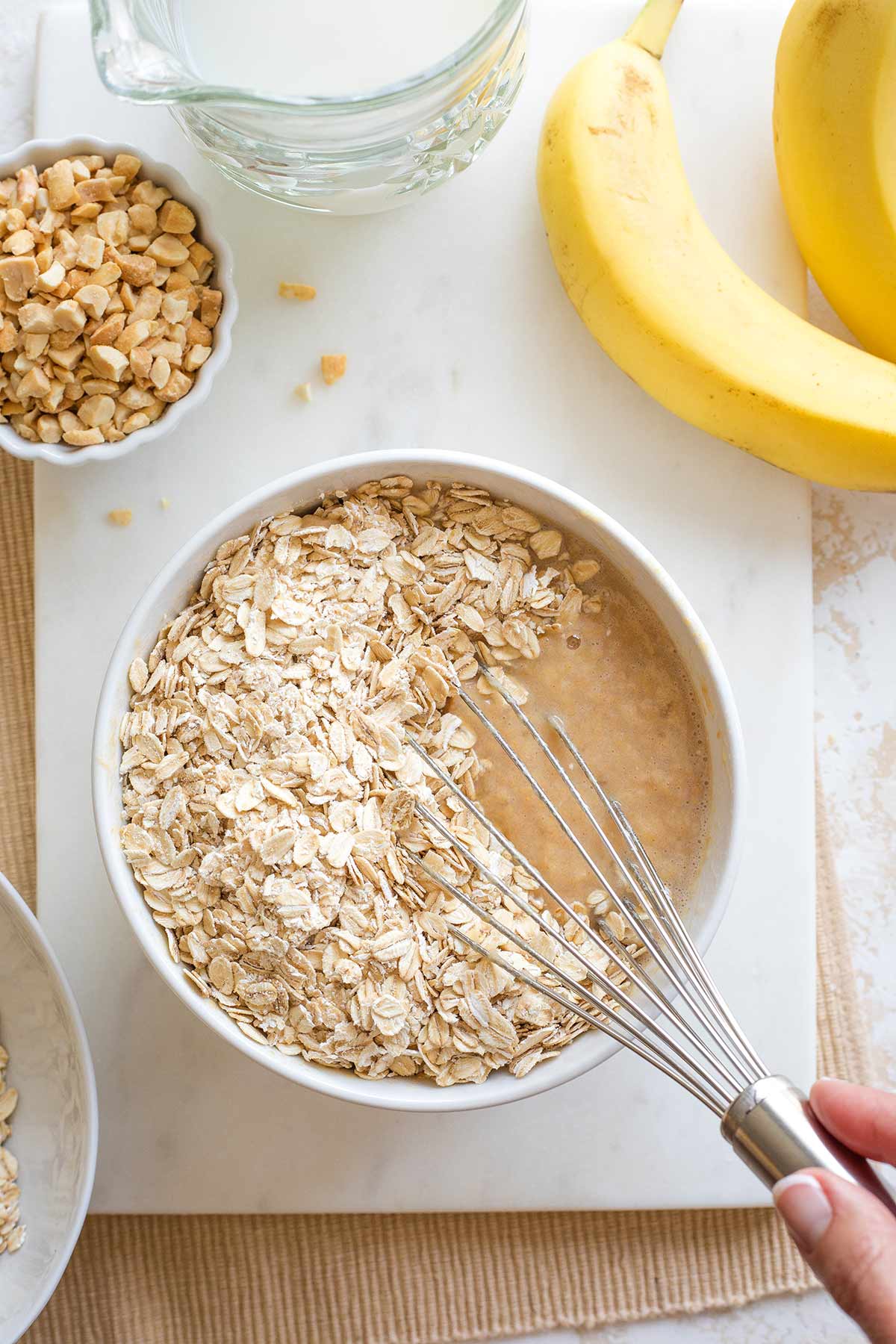 Hand holding whisk and beginning to mix oats into wet ingredients.