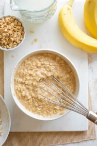 Hand holding whisk as oats are thoroughly combined into banana mixture.