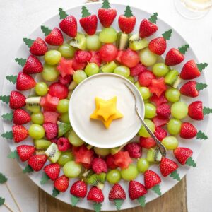 Overhead of large round plate filled with fruit kabobs arranged like a Christmas wreath around a dish of fruit dip.