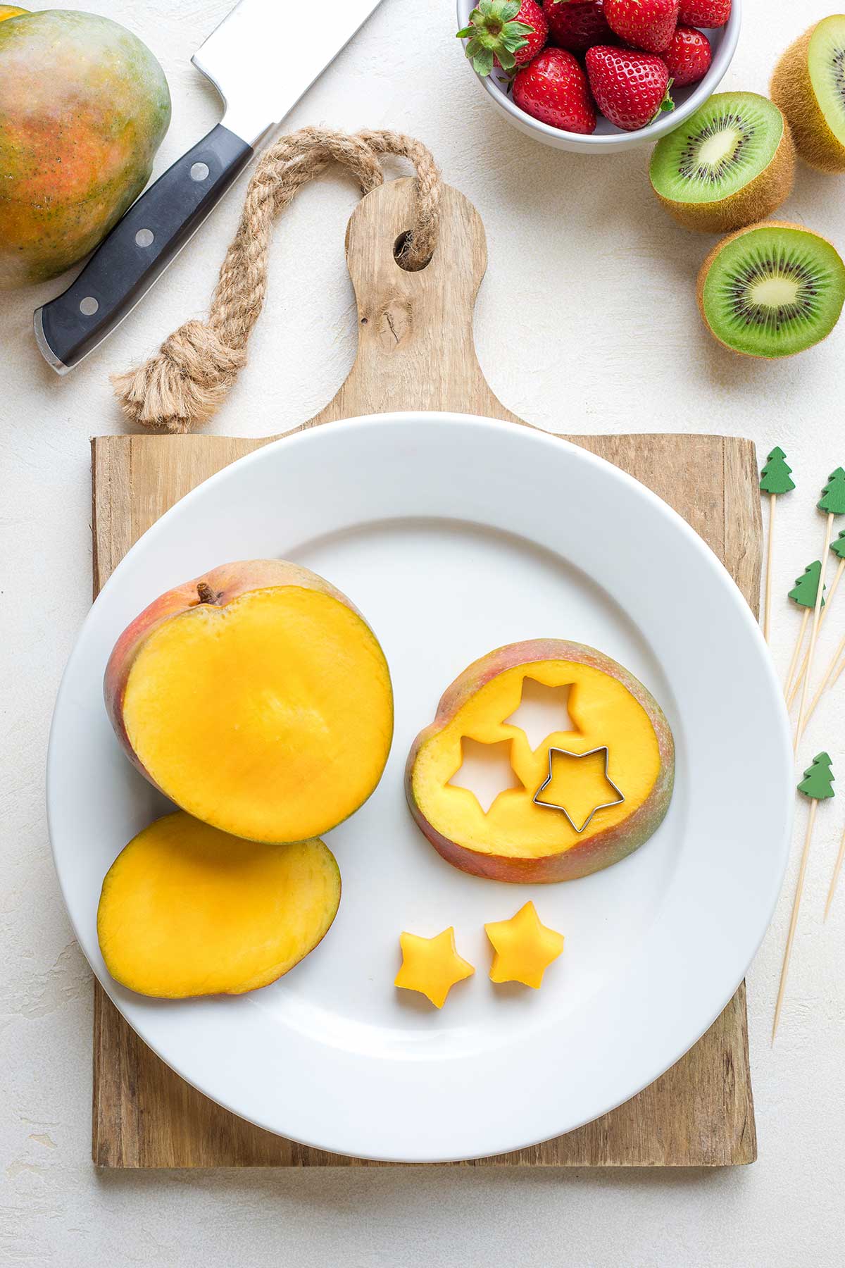 Sliced mango on white plate with small, star-shaped cookie cutter making cutouts.