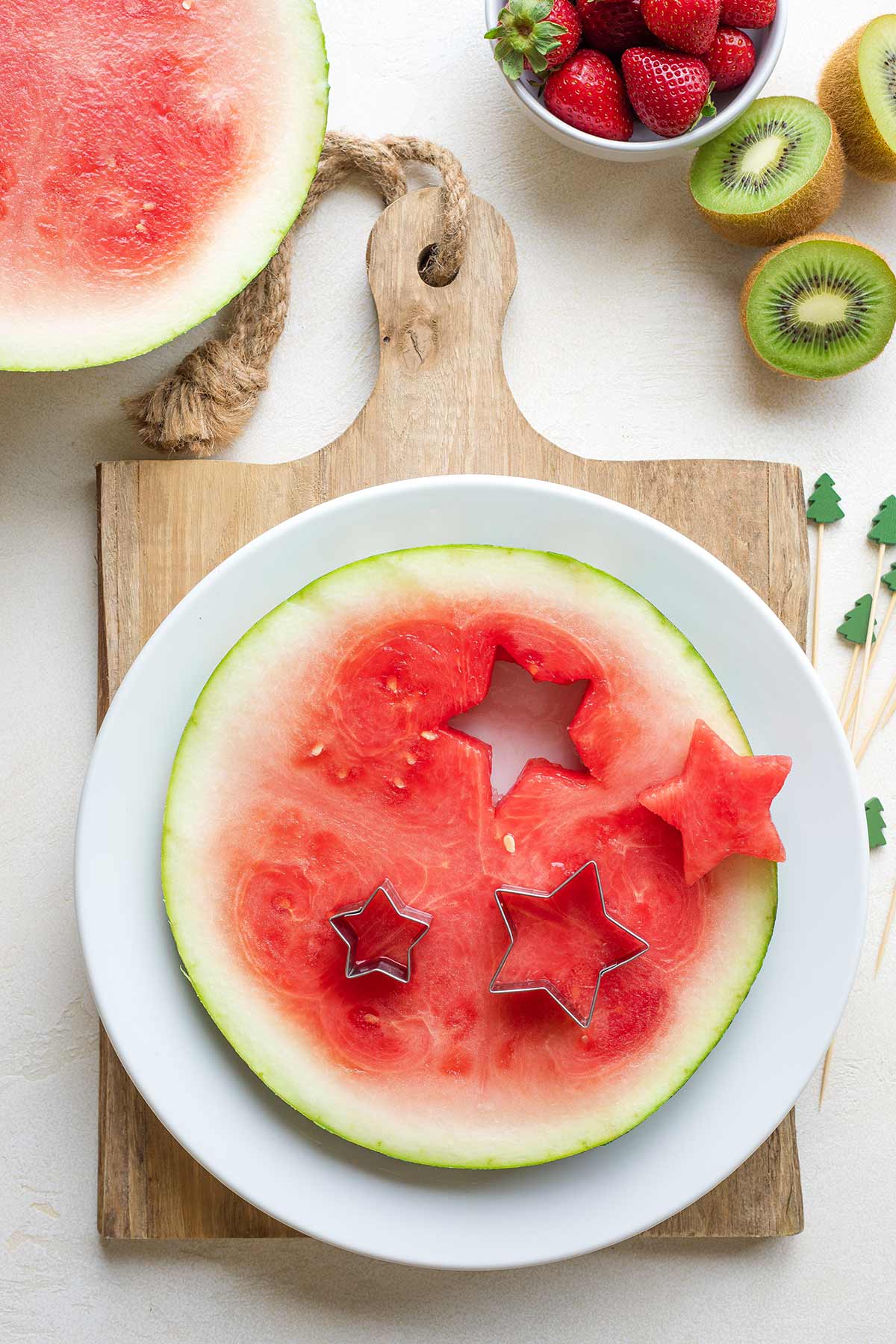 Slab of watermelon on white plate with different-sized cookie cutter cutting out star shapes.