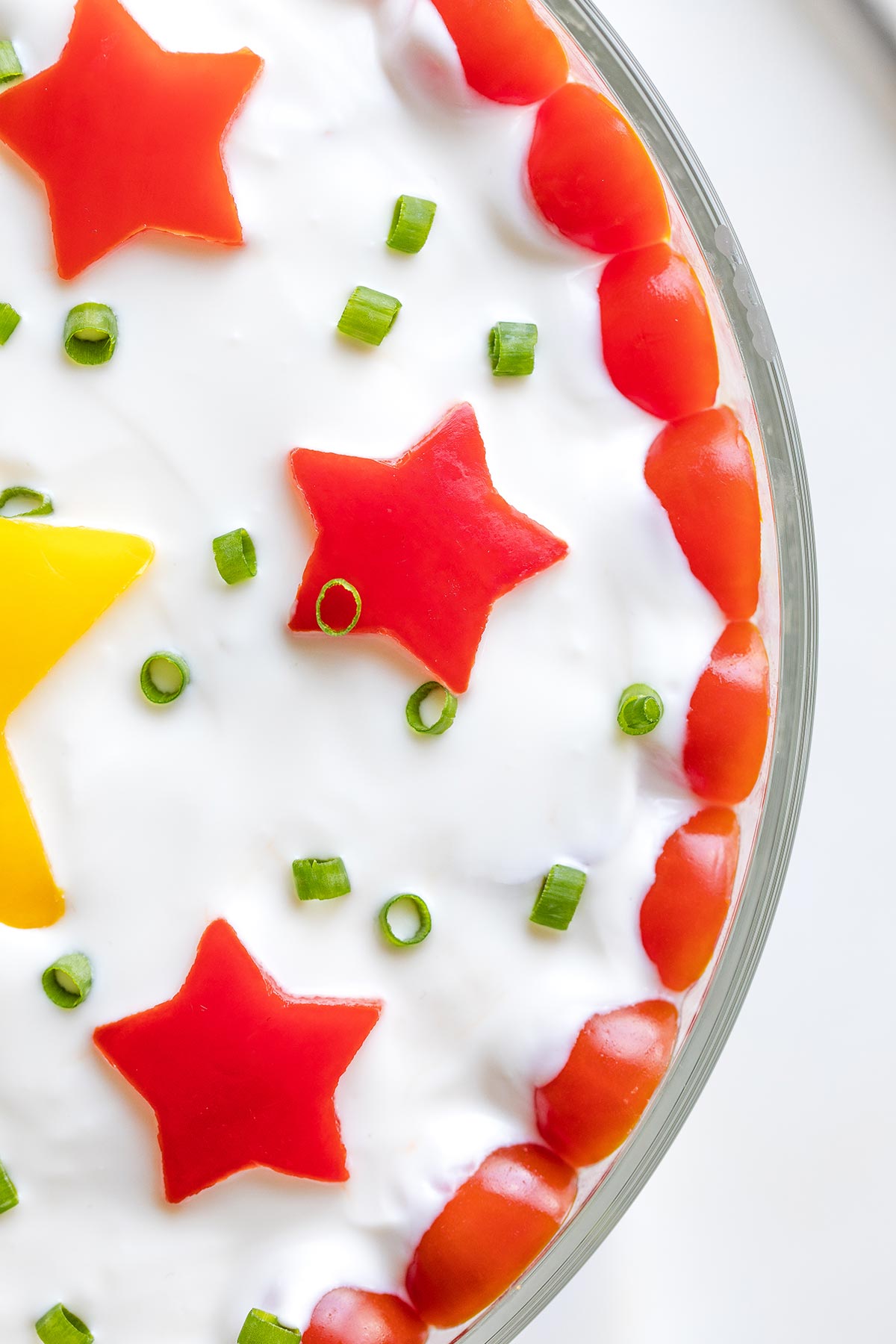 Closeup of top of salad with salad dressing and decorative pepper stars and sliced green onions.