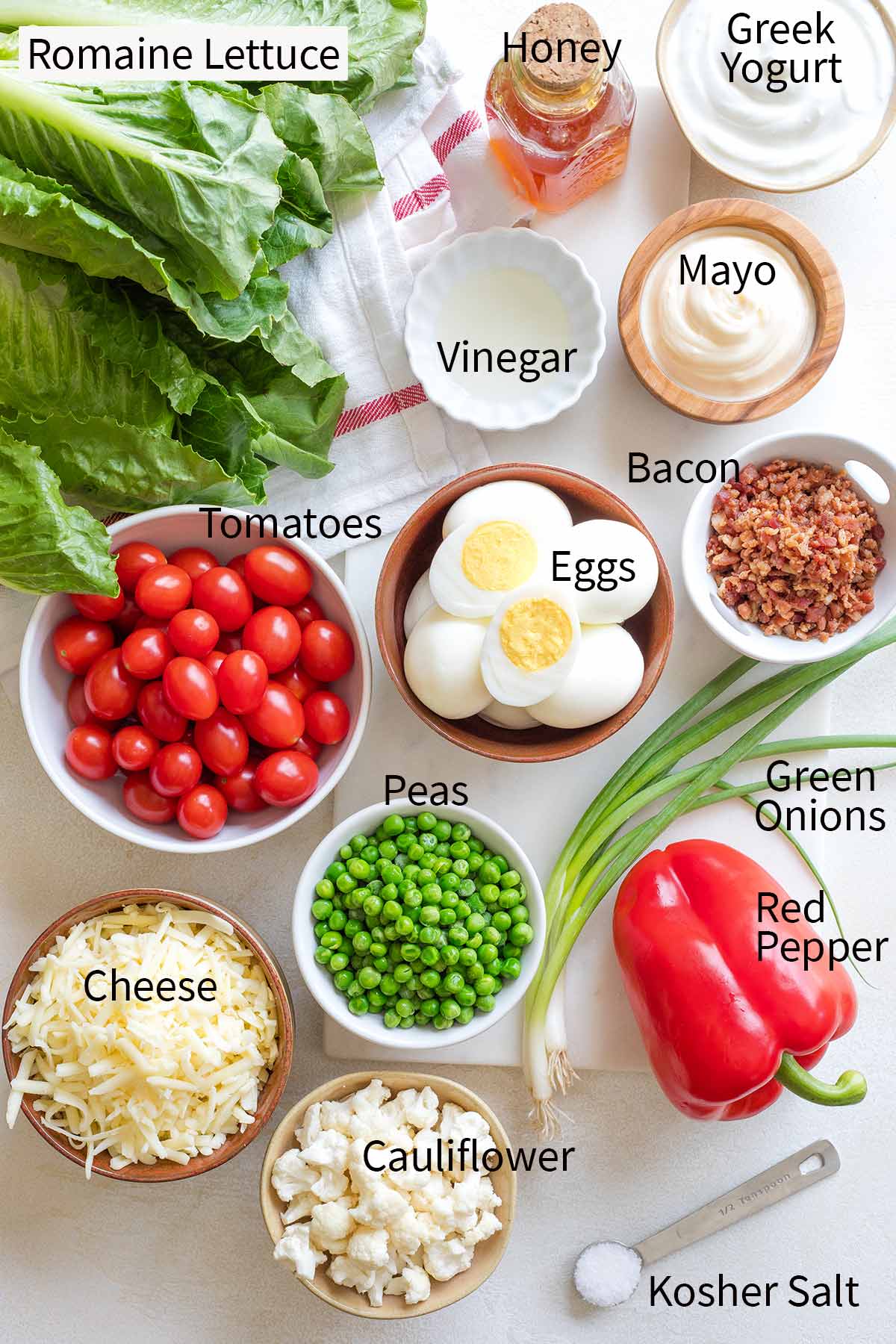 Labeled photo of ingredients: (clockwise) Romaine Lettuce, Honey, Greek Yogurt, Mayo, Bacon, Green Onions, Red Pepper, Kosher Salt, Cauliflower, Cheese, Peas, Tomatoes, Eggs, Vinegar.