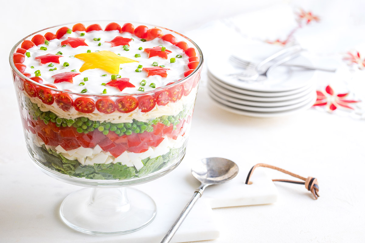 Salad on white marble cutting board with serving spoon; stack of plates in background on Christmas cloth.