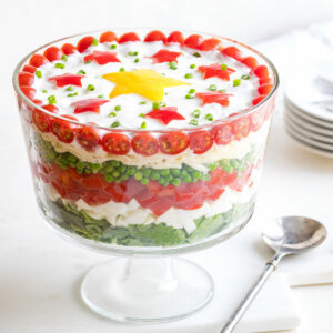 Salad in footed glass serving bowl with serving spoon alongside; plates behind.