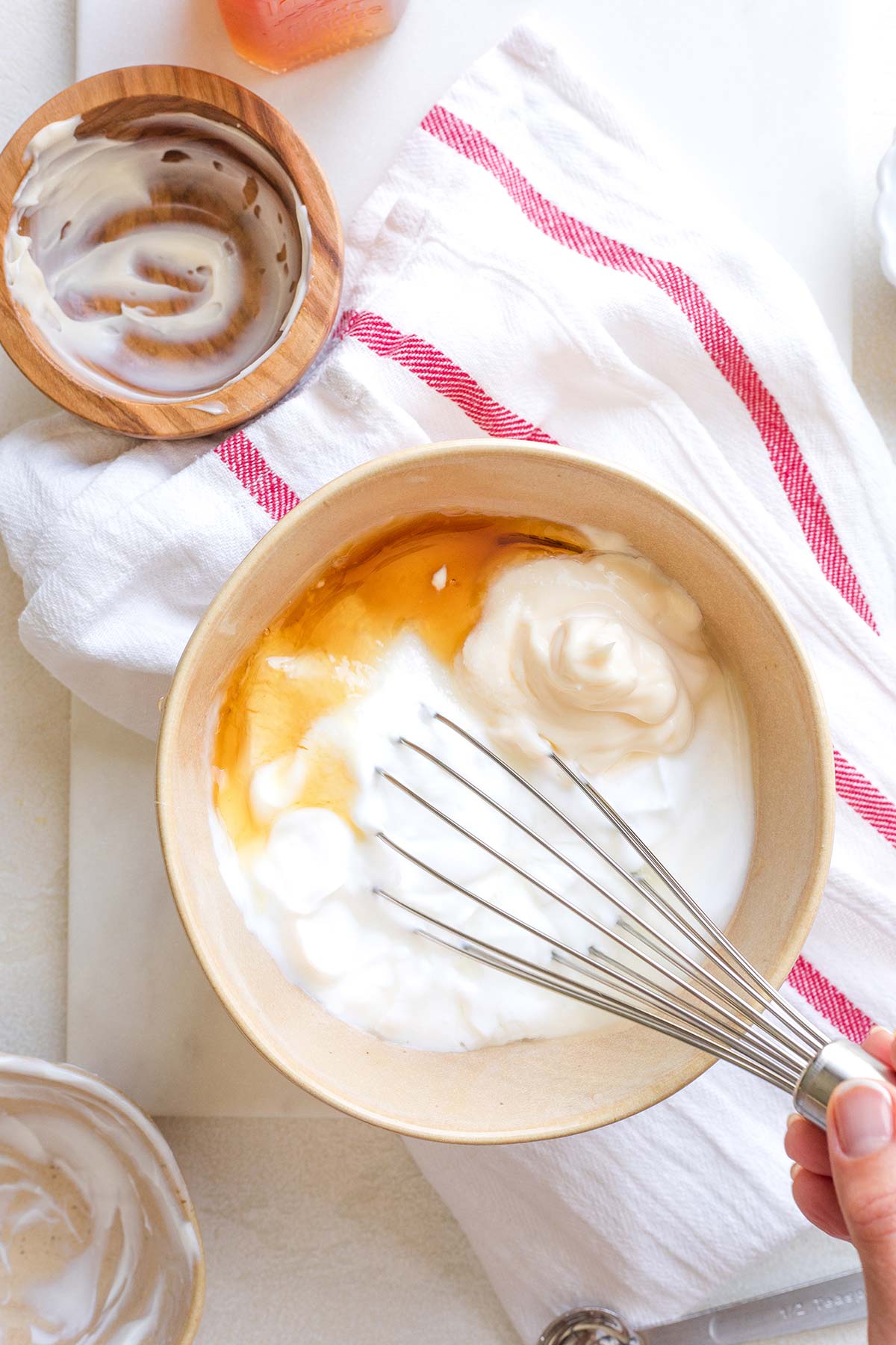 Flatlay of hand whisking together dressing; empty ingredients bowls nearby.