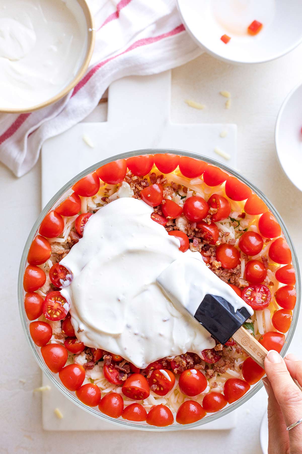 Hand spreading 7-Layer Salad Dressing on top of tomato layer.