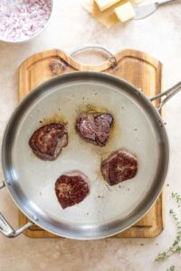 Overhead of four beef filets mignons being seared in skillet.