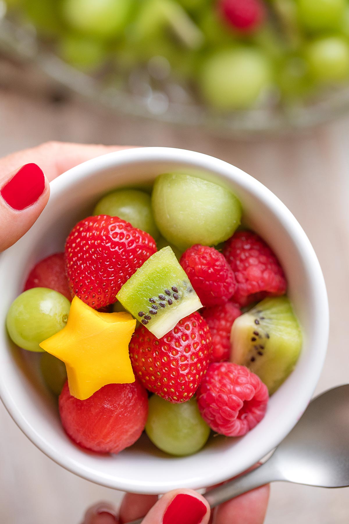 Hands holding up a spoon along with a small bowl filled with a mixture of the different fruits.