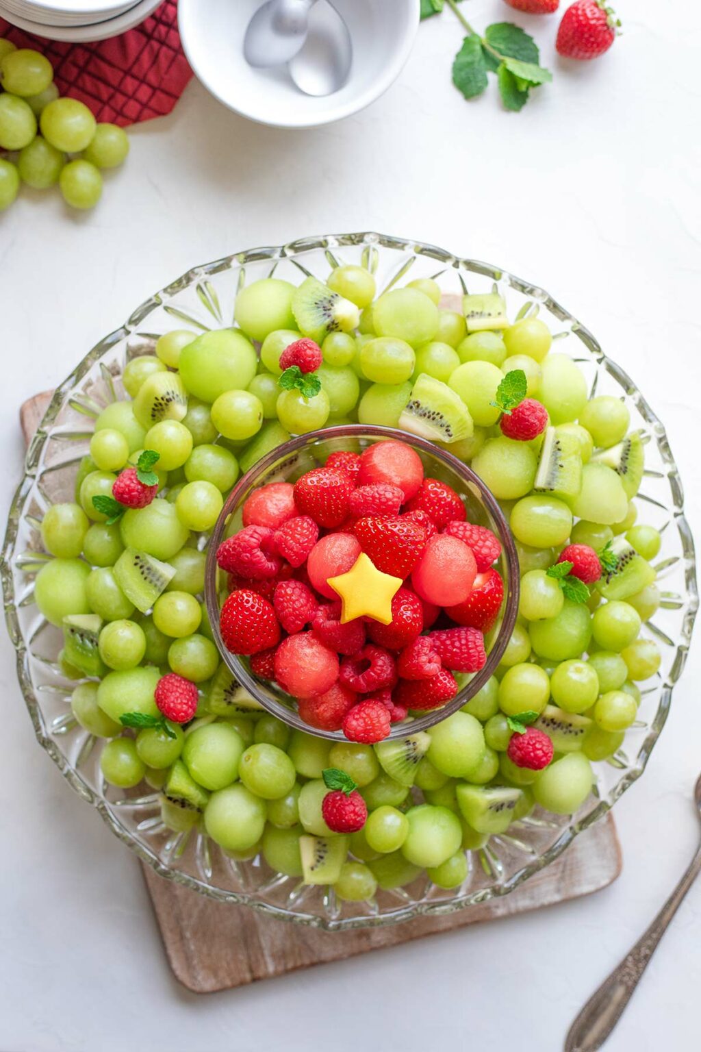 Completed Christmas fruit platter, with small mango star at the very center; extra fruit, bowls and spoons nearby.