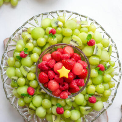 Overhead of fruit platter with extra fruit and a bowl with spoons above.