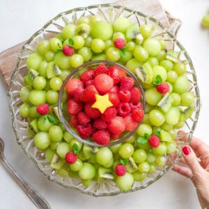 Hand grasping edge of Christmas fruit platter laying on cutting board.