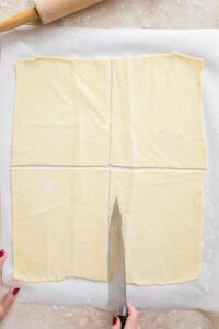 Large knife cutting puff pastry sheet into four sections.