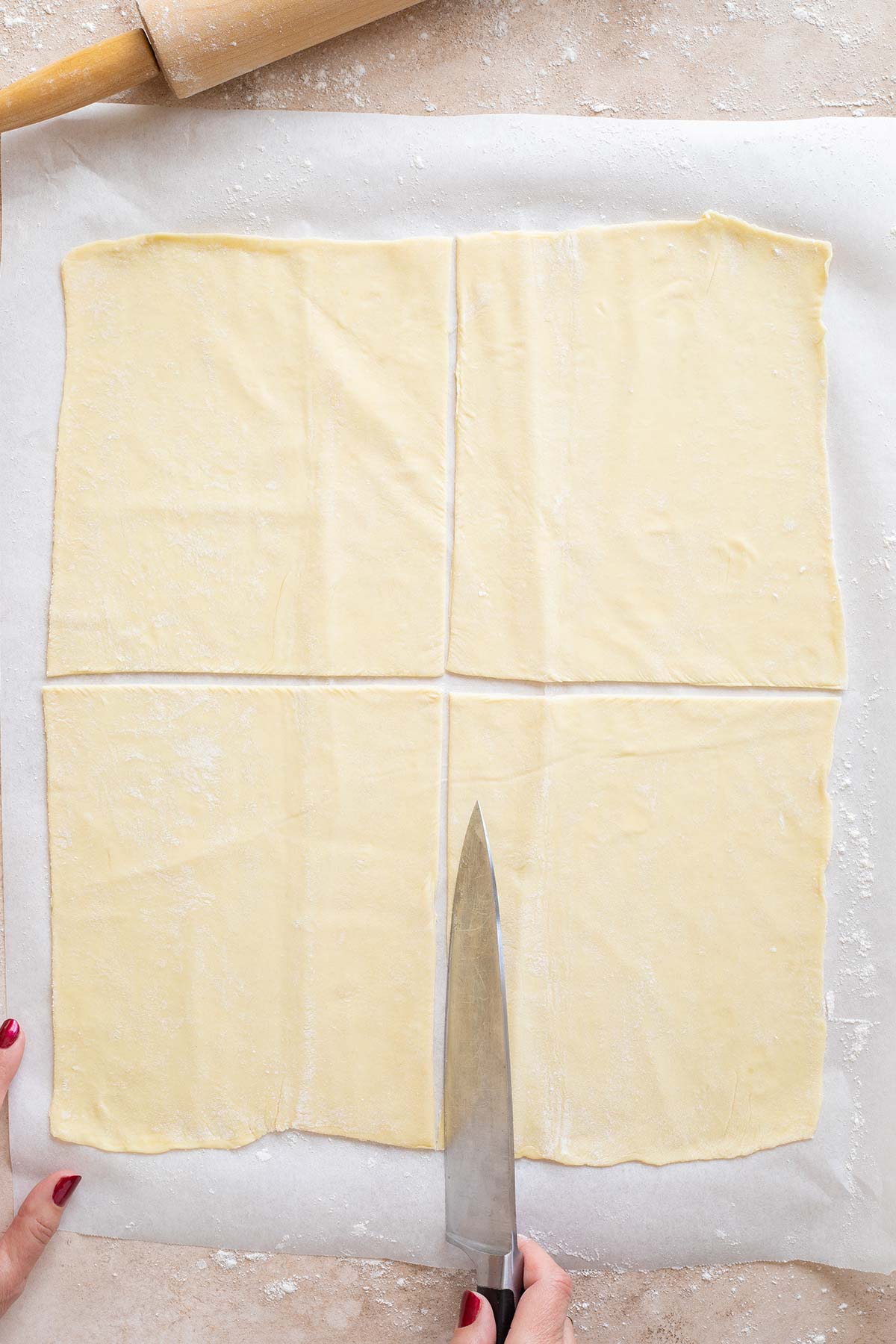 Large knife cutting puff pastry sheet into four sections.