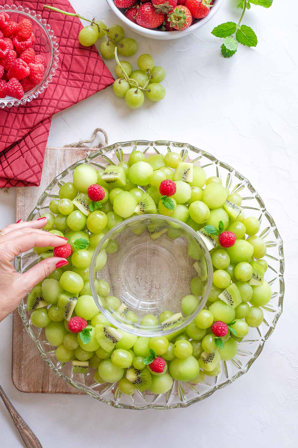 Hand adding the red raspberry accents to the the green fruit Christmas wreath.