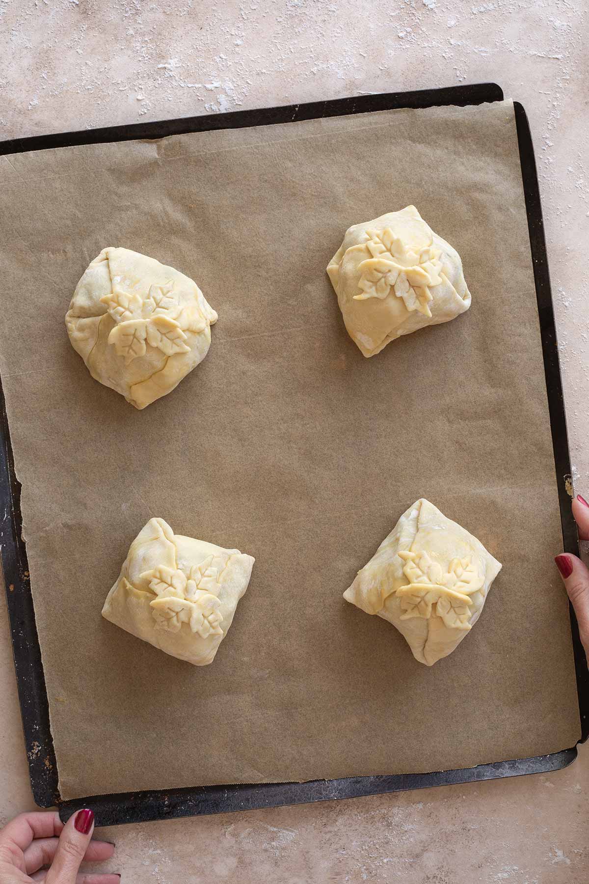 4 mini beef Wellingtons on parchment-lined baking sheet, ready to be placed in refrigerator to rest before baking.